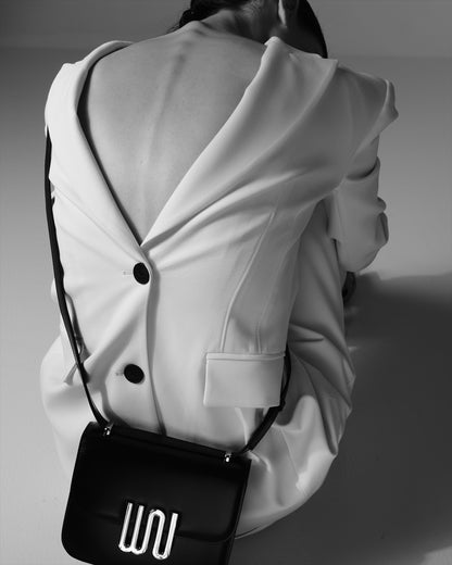 A white blazer from behind, a black crossbody resting at the hip, the WN plaque in silver.