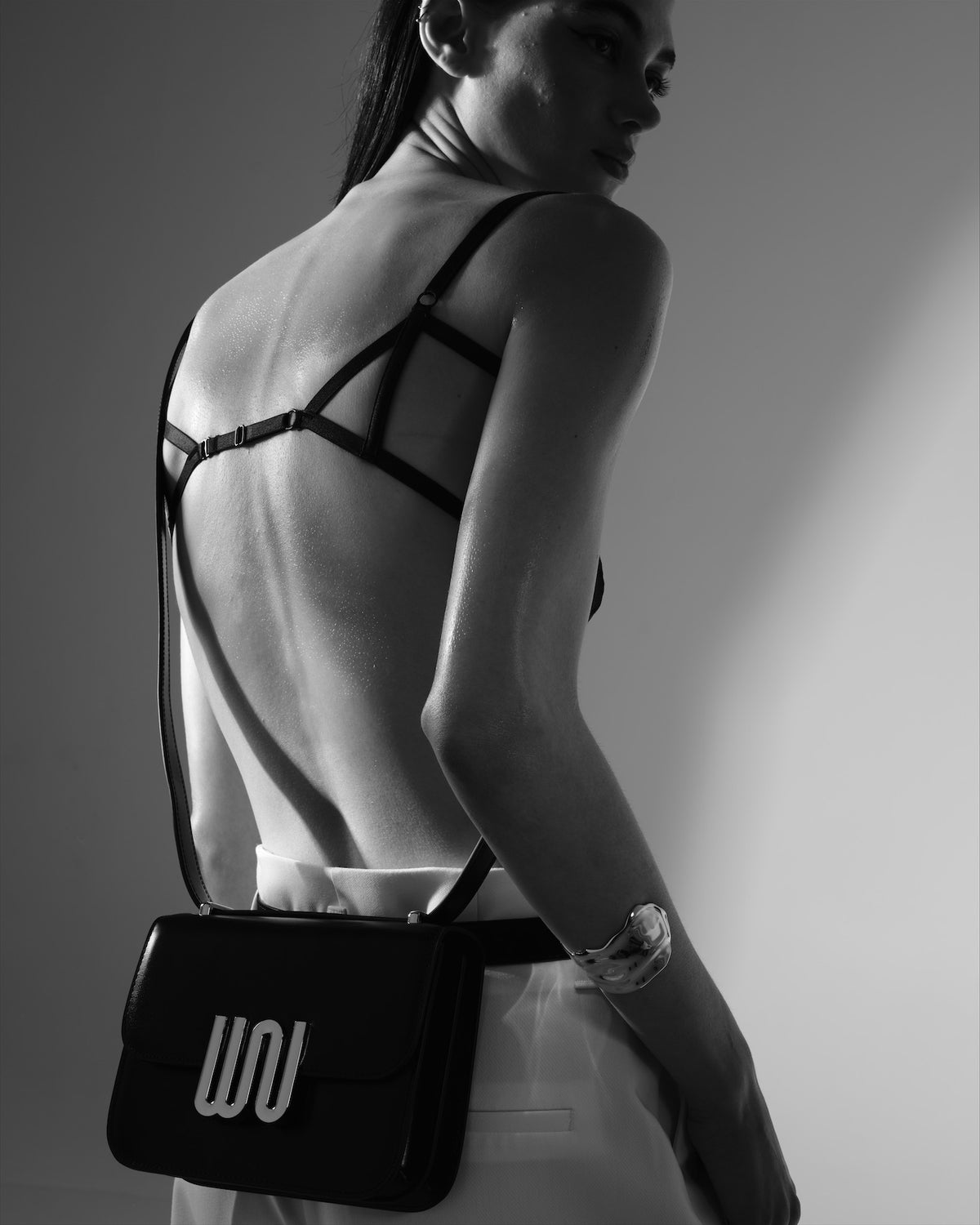 A bare back crossed by a fine harness, a black flap crossbody at the hip.