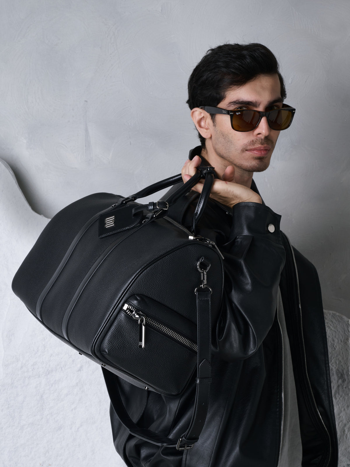 Black leather jacket and sunglasses, the black duffle with the WN tag slung over his shoulder