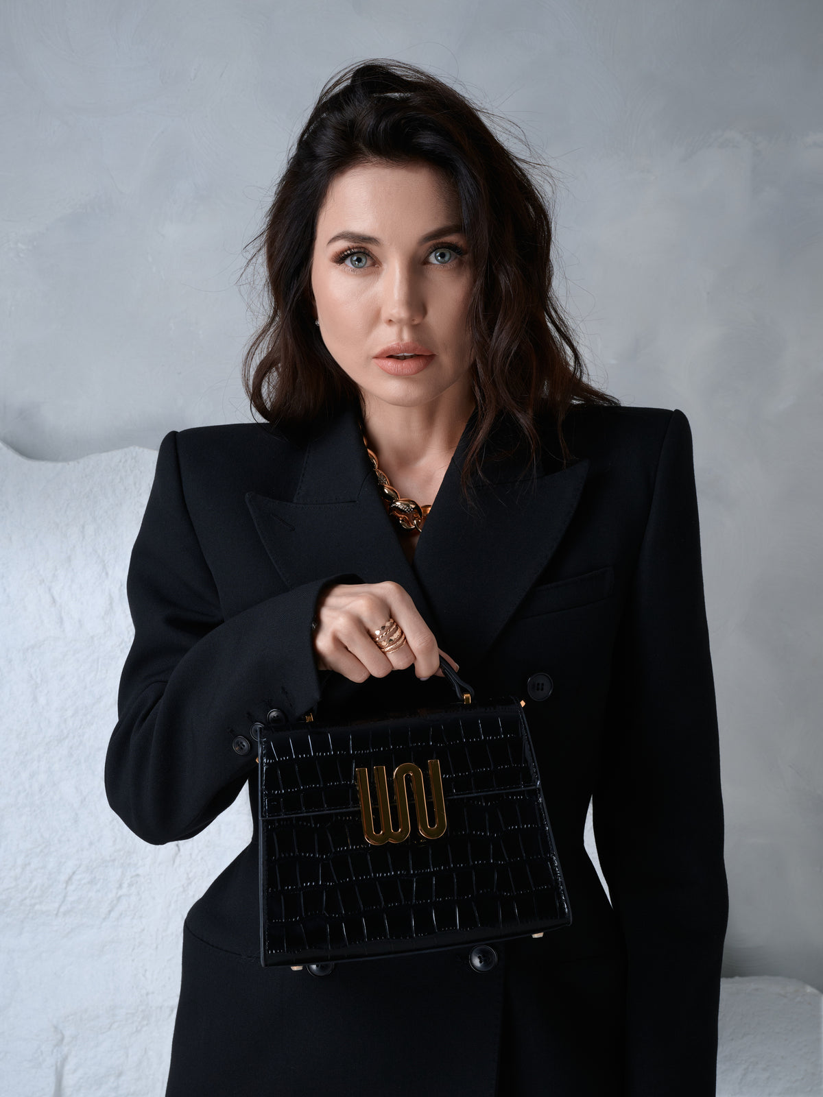 Bronzite Noir held by its top handle against a black double-breasted coat, looking into camera
