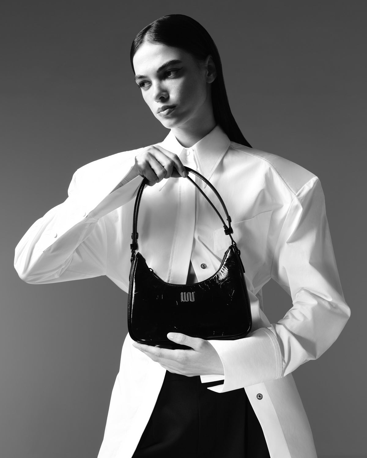 Black and white: a woman in a sculptural white shirt holding a black patent White Noise The Label bag with the WN